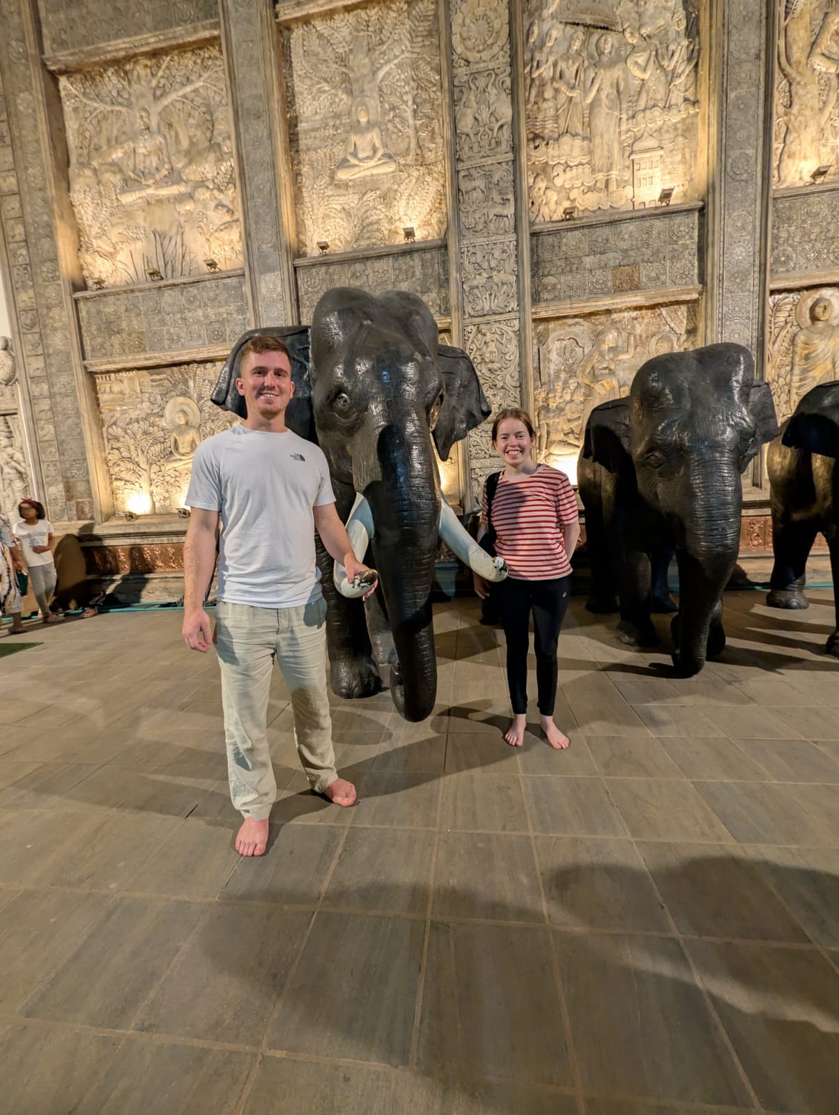 Two guests beside elephant displays and carved temple panels