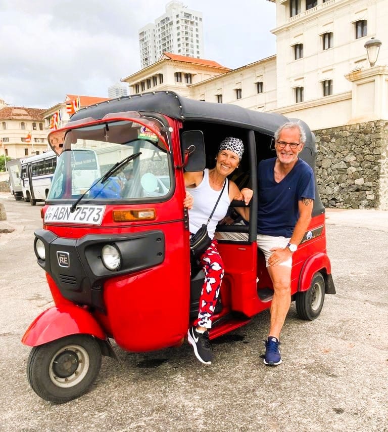 Two guests in a red tuk tuk outside a historic white building